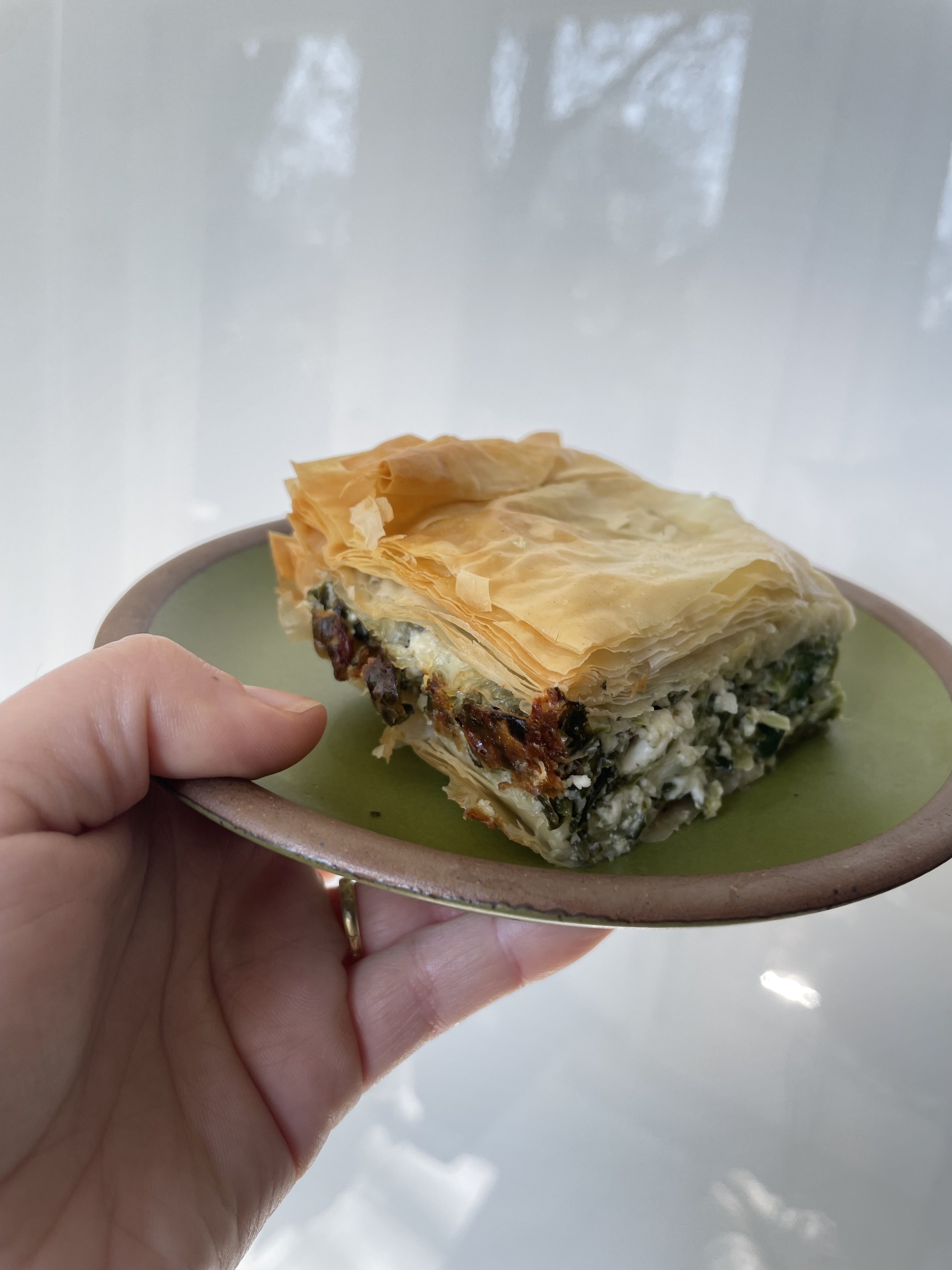 A photo of Antigoni's hand holding a slice of the spanakopita she made. It looks supremely delicious.