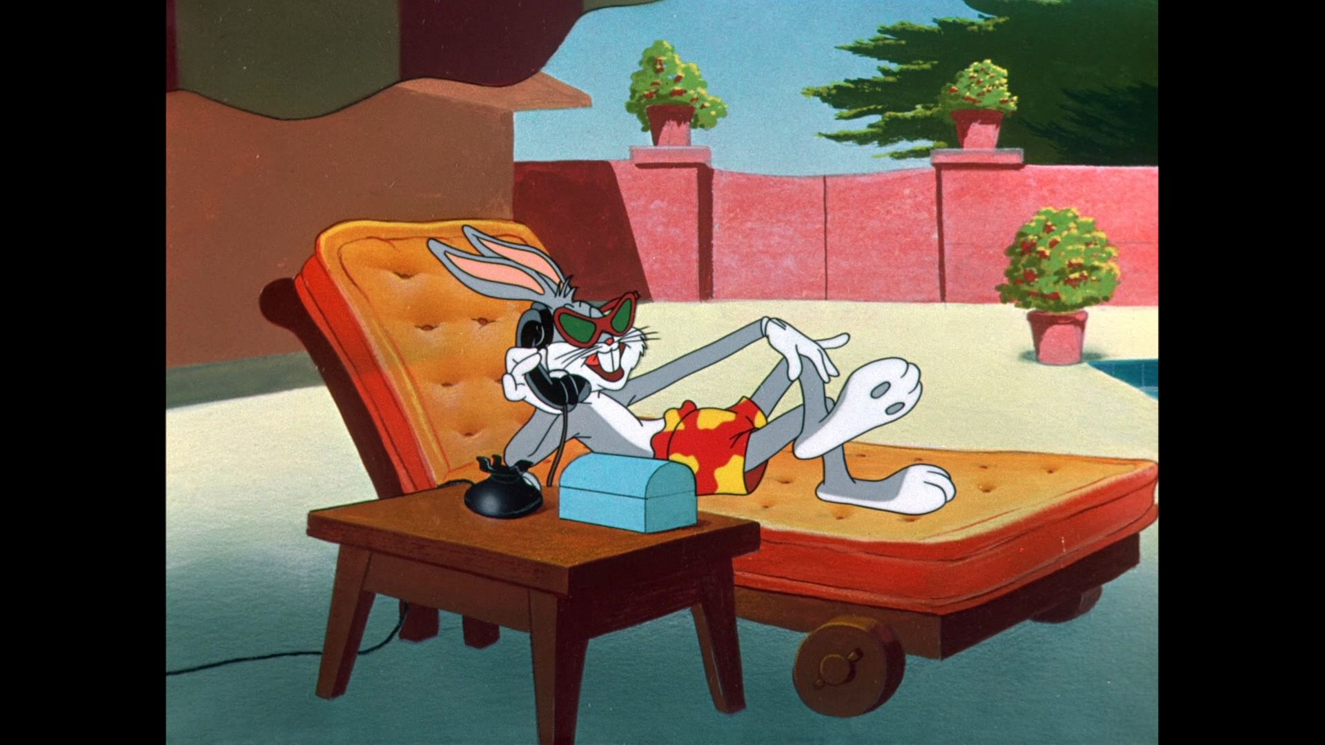 A still shot from a Looney Tunes Cartoon. Bugs Bunny lies back on a poolside plush orange beach chaise. He's wearing cat-eye sunglasses and patterned swim shorts, and is grinning as he speaks into an old-fashioned corded telephone set up on a table beside him. In the background he's surrounded by a brick wall and some fancy potted plants.