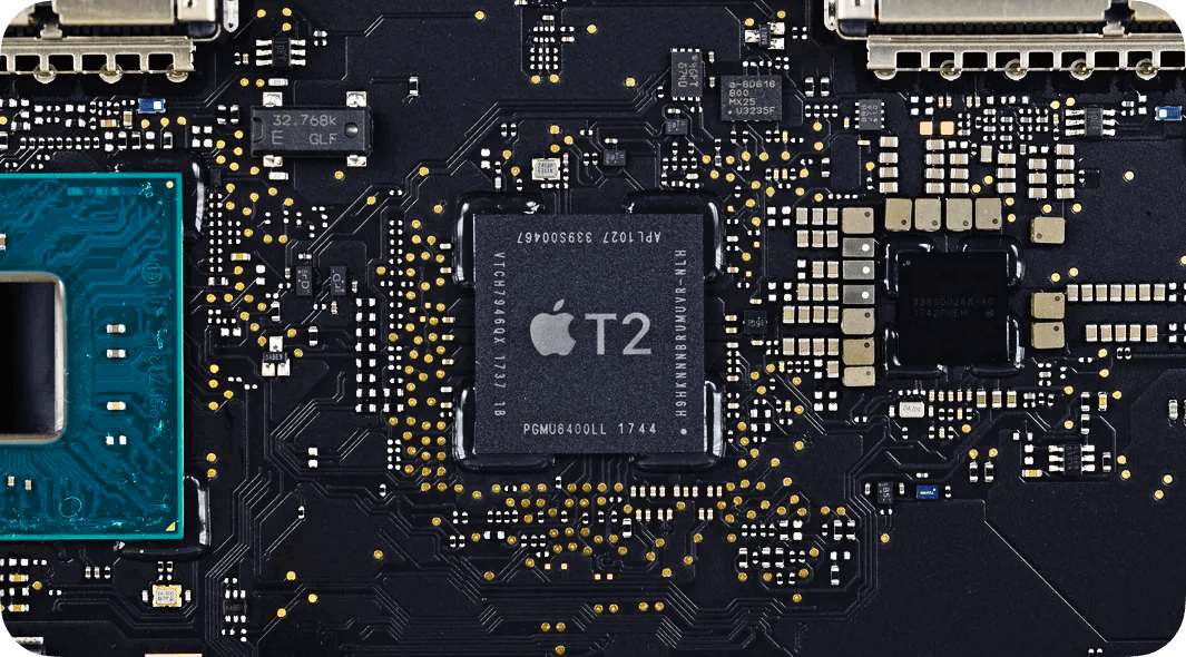 A macro photograph of a Mac logic board with the T2 chip centered